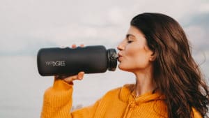 A woman drinking from a black water bottle for her portfolio.