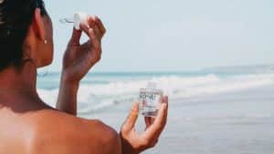 Eine Frau hält eine Flasche KONU-Kosmetik-Sonnencreme am Strand.