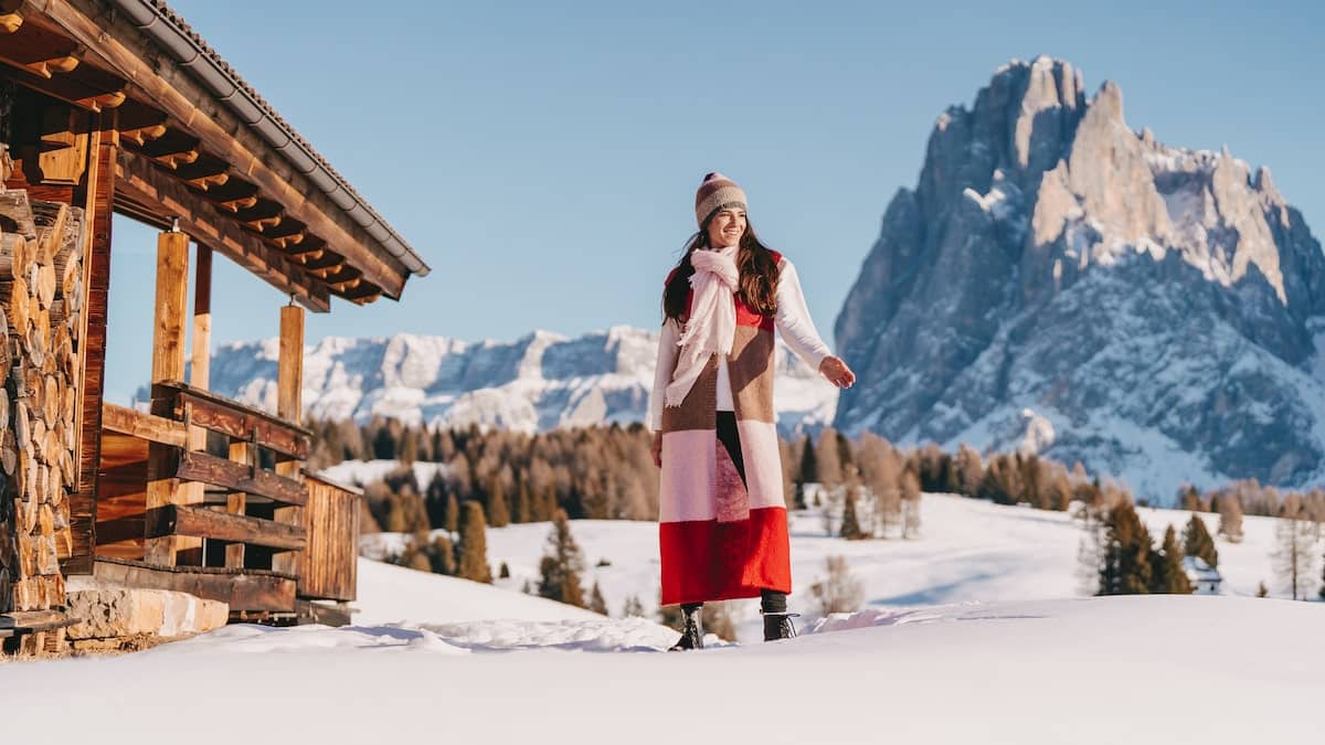 A woman standing in front of a snowy cabin.