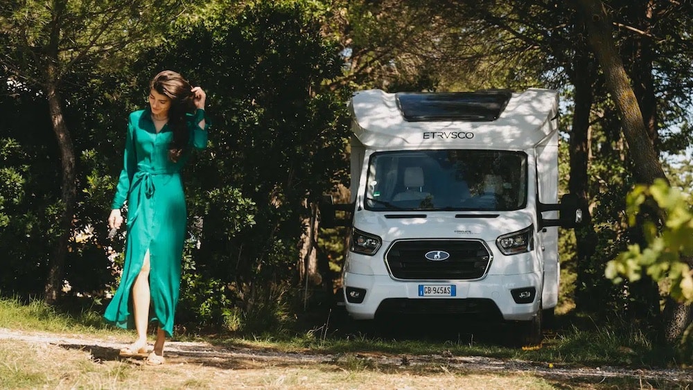 A woman in a green dress standing next to an Etrusco Italy camper van.