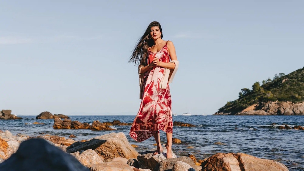 Eine Frau in einem langen Kleid steht auf Felsen am Meer und sieht aus wie aus einem italienischen Gemälde.