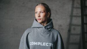 Eine Frau trägt einen grauen Kapuzenpullover mit dem Wort „Complete“ darauf.