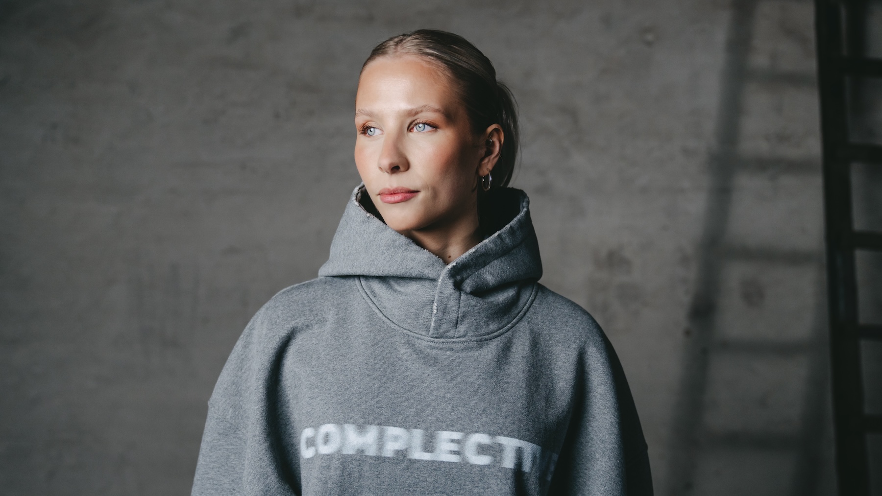 Eine Frau trägt einen grauen Kapuzenpullover mit dem Wort „Complete“ darauf.